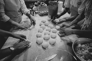 Close up of a group of hands rolling dough.