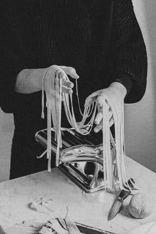 A close up on hands making pasta with a pasta maker.